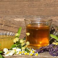 Cup Of Hot Aromatic Tea, Honey And Different Fresh Herbs On Wooden Table
